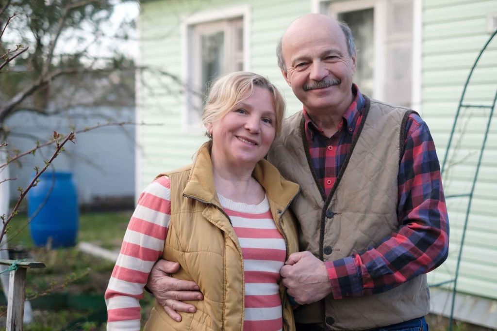 Older couple standing in front of their home, smiling for a photo