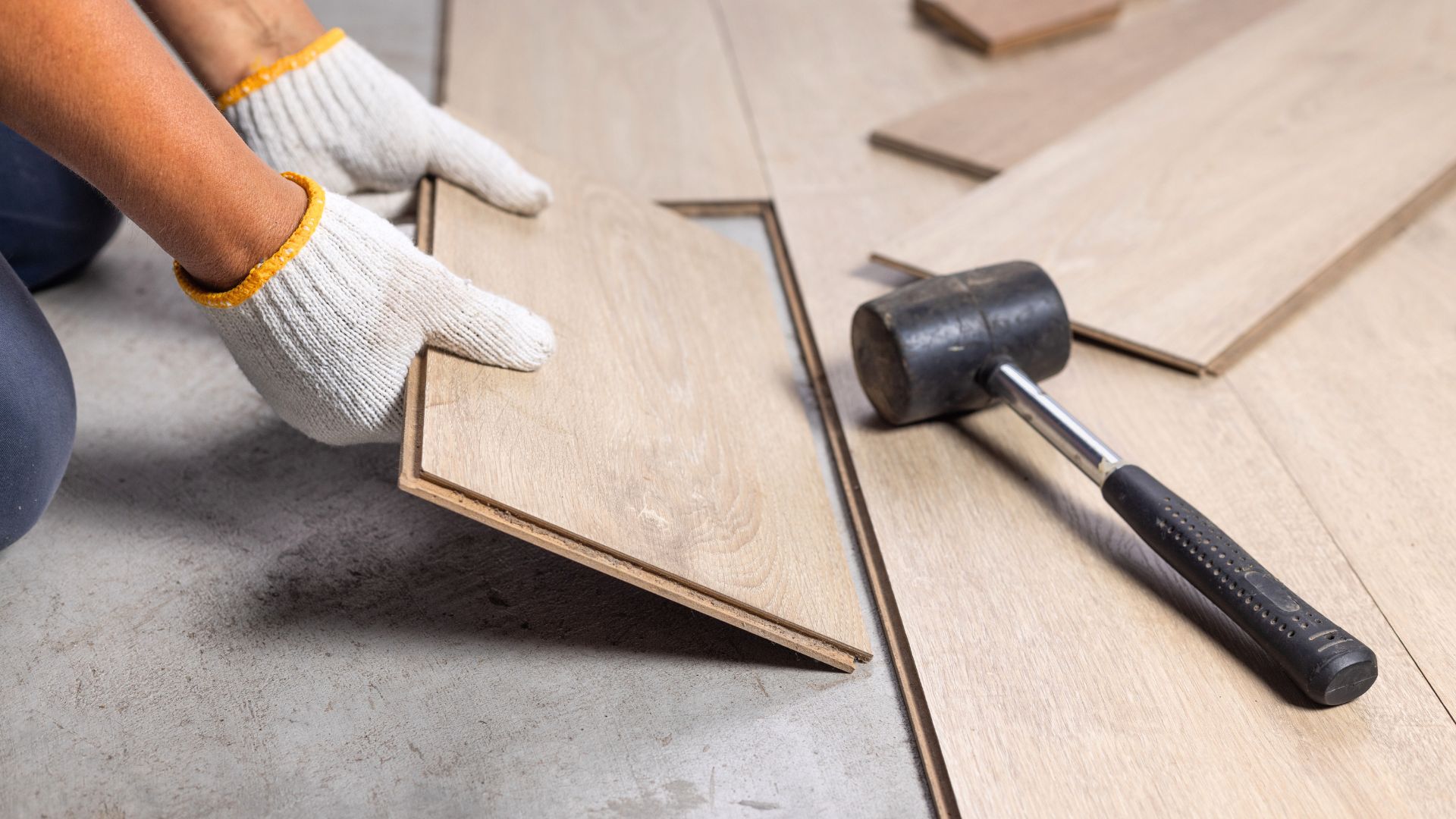 Close up of gloved hands installing wood floor planks
