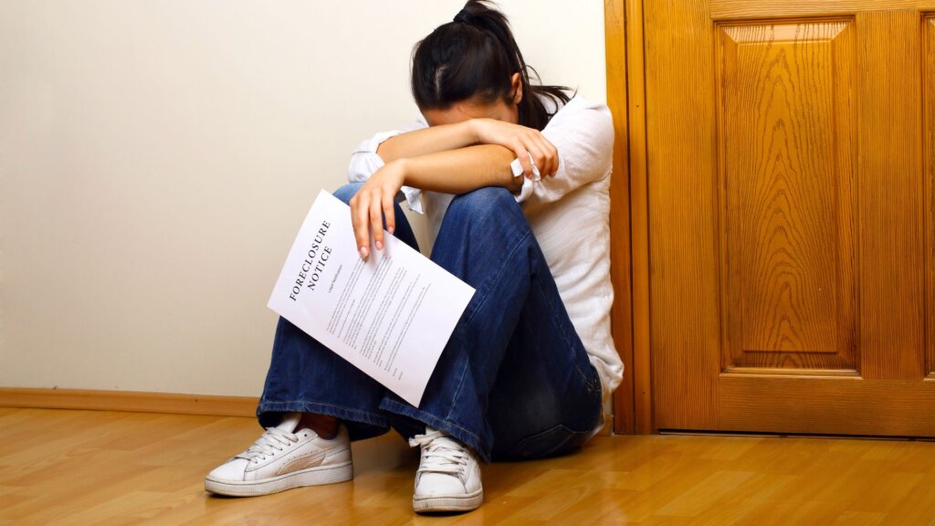 Homeowner sitting on floor holding foreclosure notice