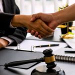 Handshake over legal documents with judge’s gavel on desk
