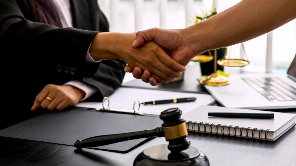 Handshake over legal documents with judge’s gavel on desk