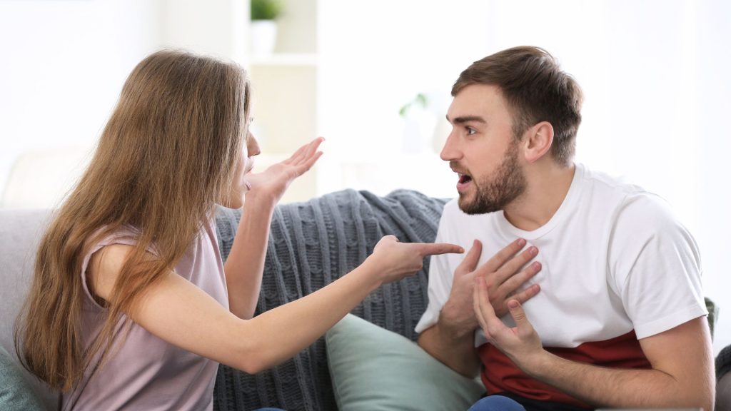Woman gesturing angrily at man on couch