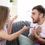 Woman gesturing angrily at man on couch