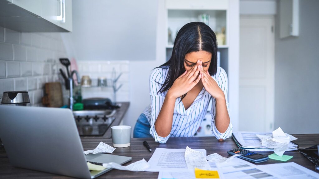 Woman reviewing bills at kitchen counter looking stressed