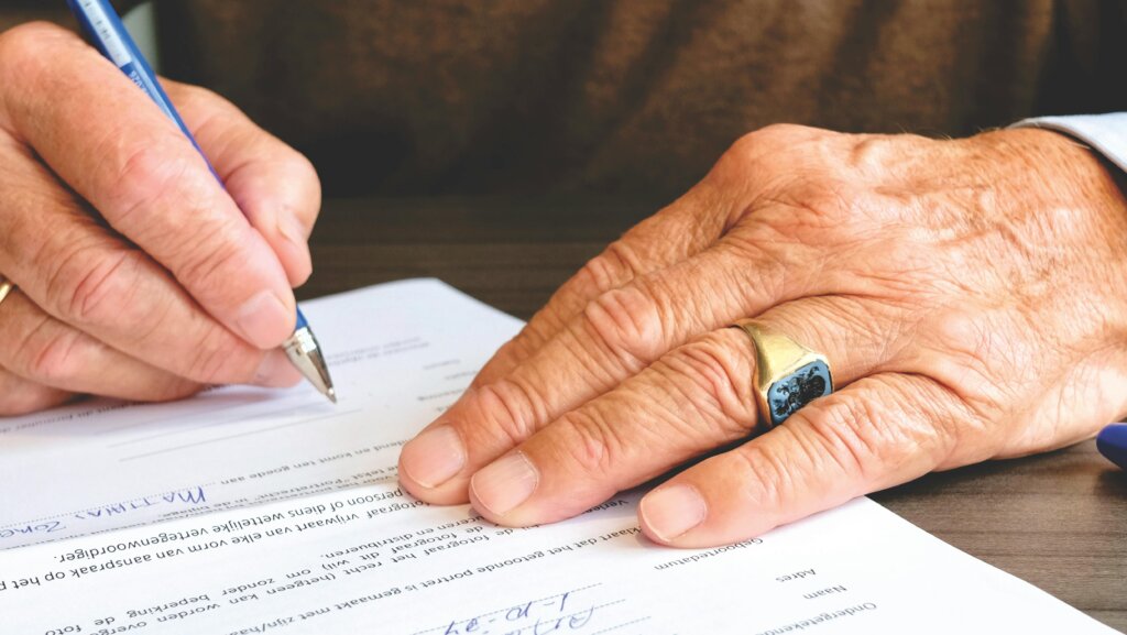 Close up of older person signing document with pen