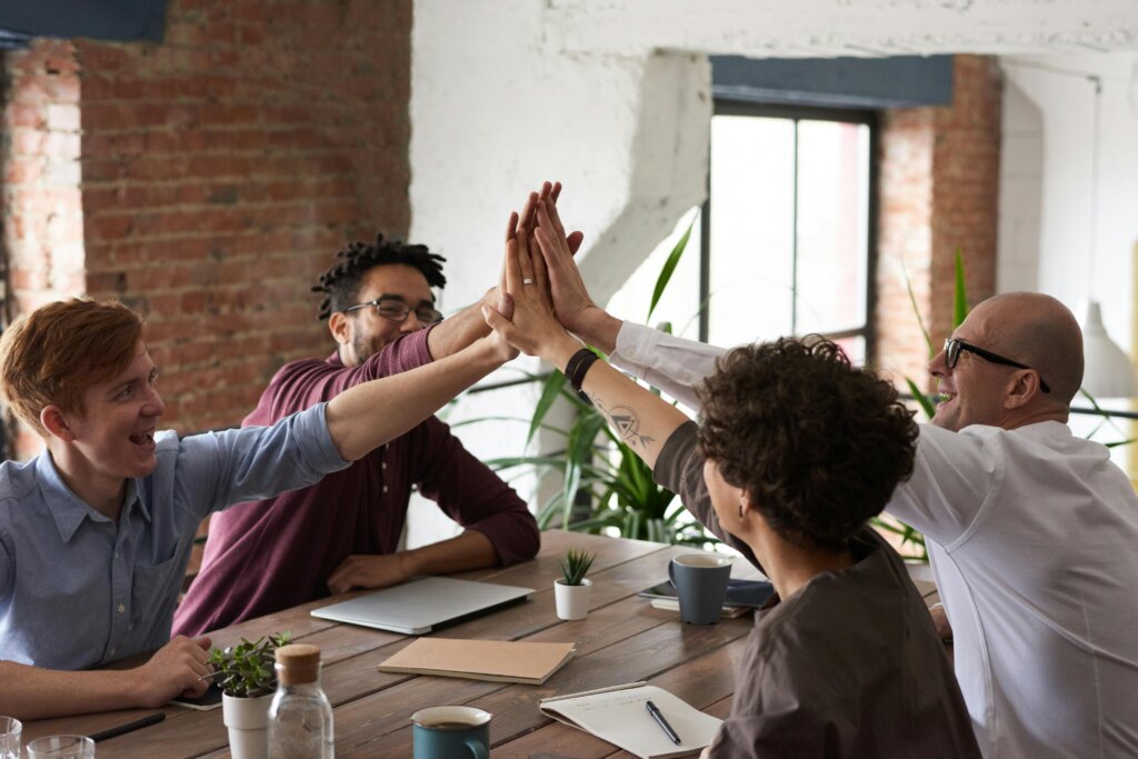 Four people high fiving at table with paperwork and laptop